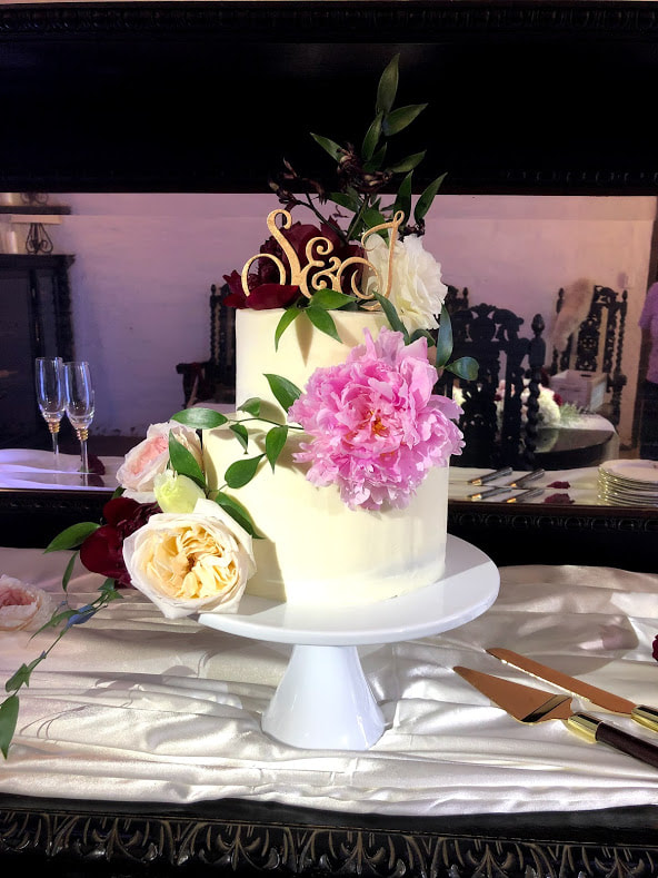 Picture of a two-tier wedding cake, with satin linen, white porcelain stand on a dark wood antique table at the Redlands Assistencia