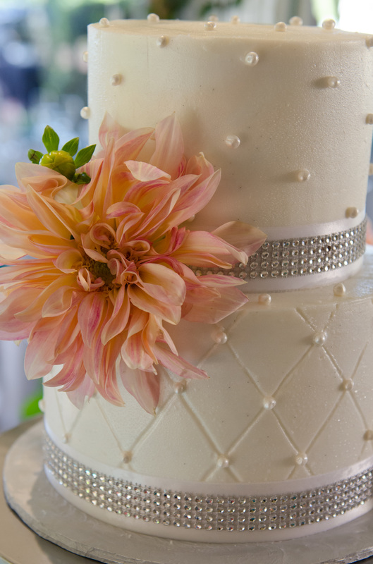 Picture of a small two-tier wedding cake with a peach-colored dahlia, pearl and faux diamond accents