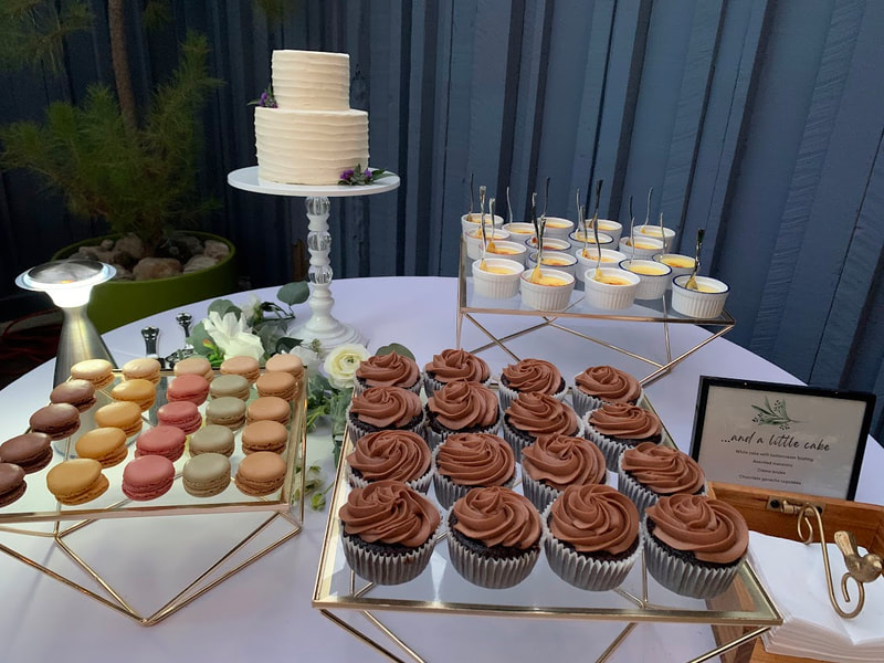 Picture of mini cutting cake on tall stand with three geometric glass and gold stands, each holding a mini desserts: macarons, chocolate ganache cupcakes and mini creme brulee