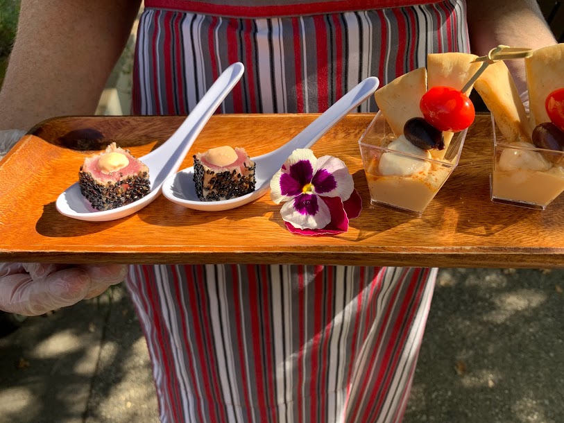 Chef holding a tasting board with two each of sesame-seared ahi with sriracha mayo, mezze shots with house-made hummus, pita chip and caprese skewer