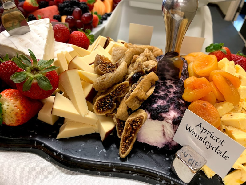 Picture of dried figs, dried apricots, fresh strawberries and cheeses: smoked gouda, brie, blueberry chevre and apricot wensleydale on a black board