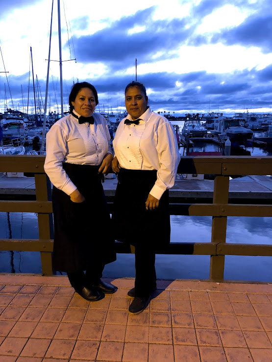 Staff members standing in front of a wooden railing at a dock with sailboats