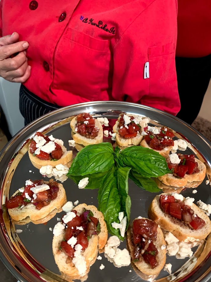 Chef holding a tray of bruschetta with a fresh basil leaf garnish