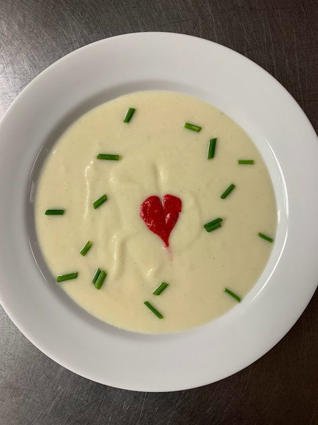Picture of a bowl of soup: vichysoisse with chives and heart-shaped garnish of spicy borscht